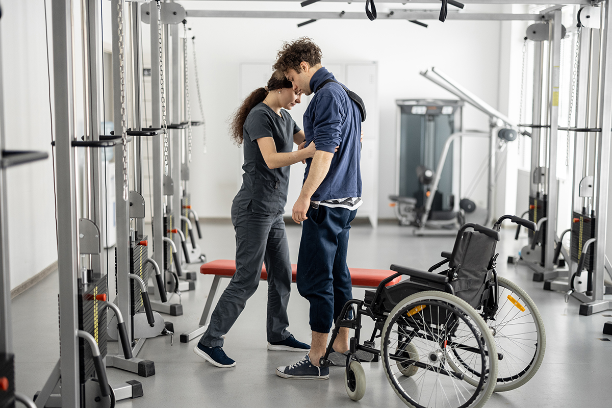 Rehabilitation specialist helps a guy stand out of a wheelchair